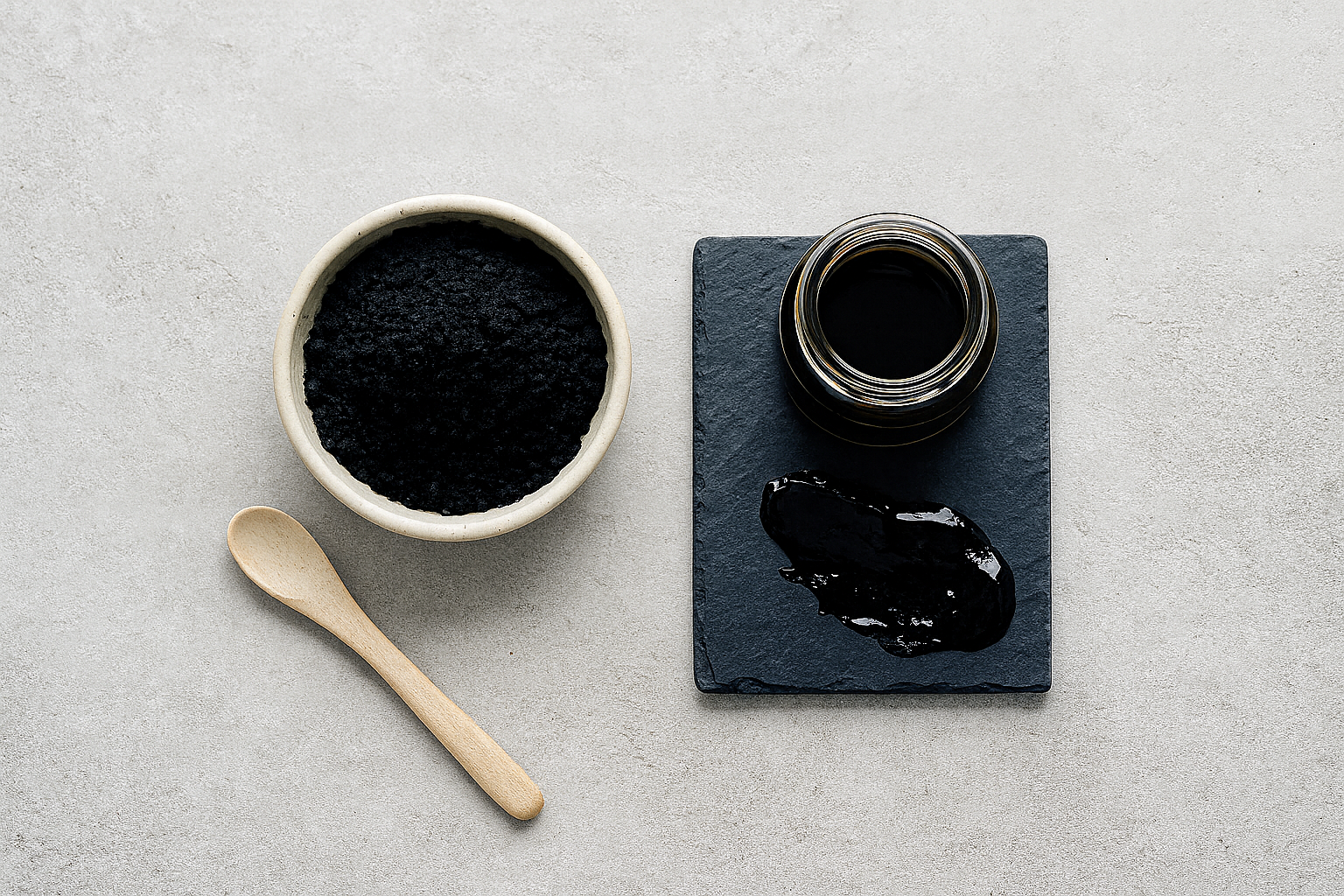 Shilajit (Mumijo) als Harz und Pulver auf grauem Hintergrund: Schälchen mit Pulver, kleine Glasdose mit Harz auf Schieferplatte, Holzlöffel daneben – geeignet für den Abschnitt „Woraus besteht Shilajit?“.
